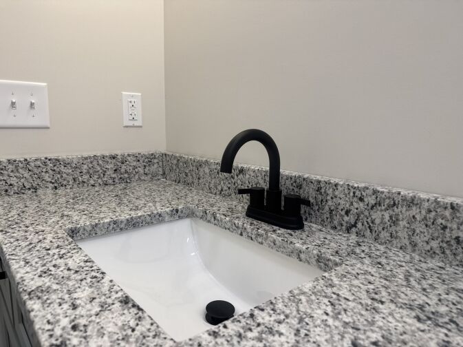 Granite bathroom countertop with an undermount sink, matte black faucet, and nearby light switch and outlet on a beige wall.