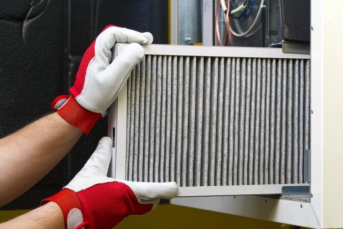 Person wearing red and white gloves installs or removes a pleated air filter from a residential HVAC system.