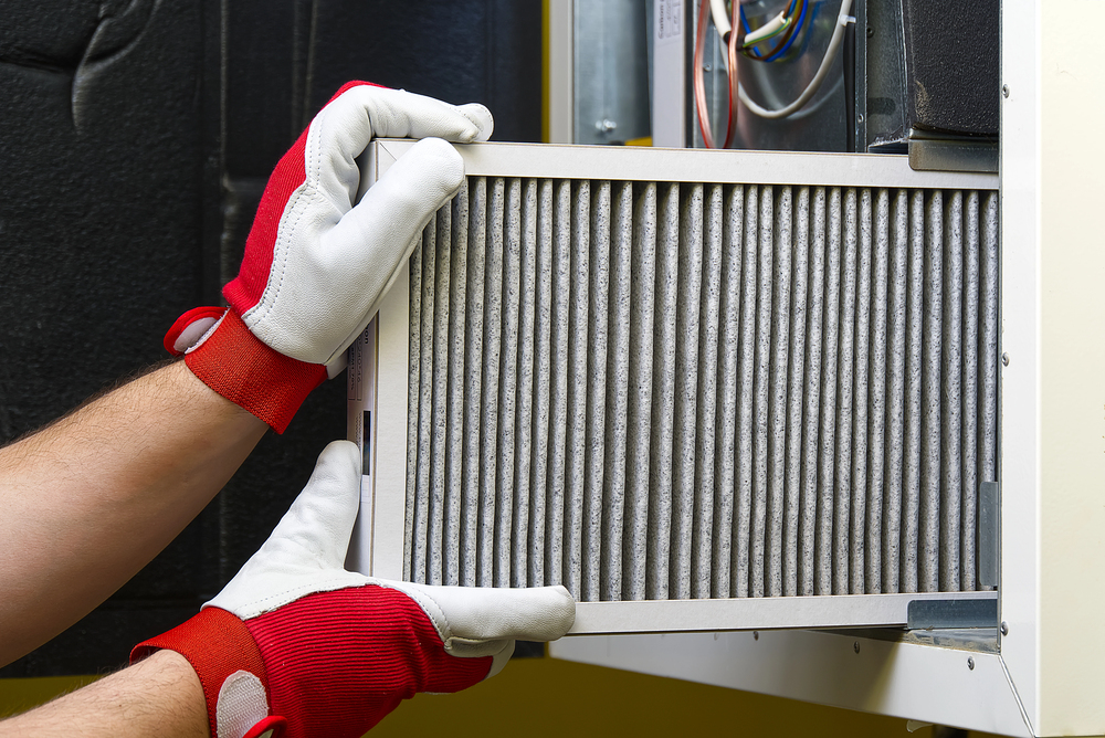 Person wearing red and white gloves installs or removes a pleated air filter from a residential HVAC system.